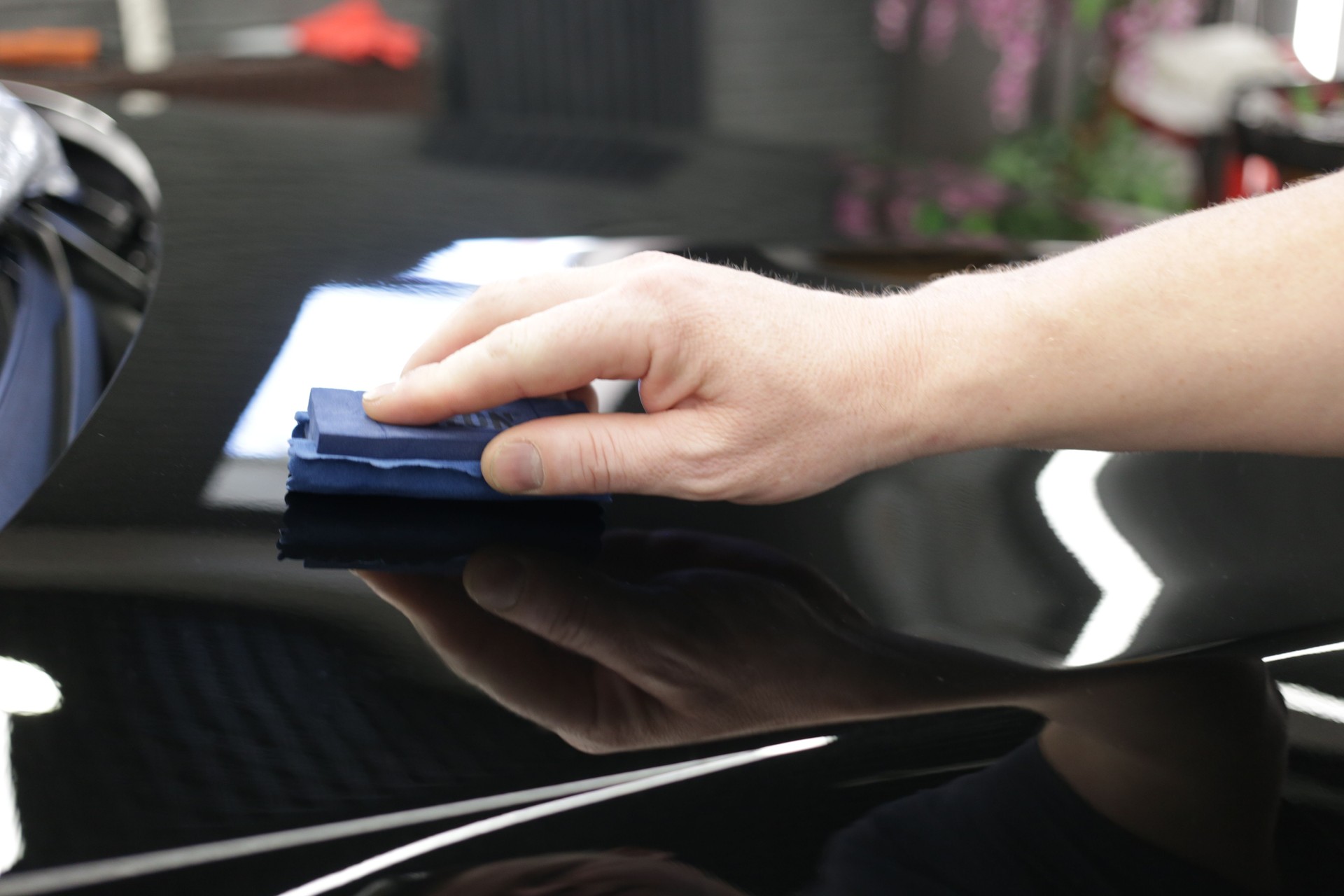 Car service worker applying nano coating on a car detail close-up. Closeup of hand coating black car bonnet paint.