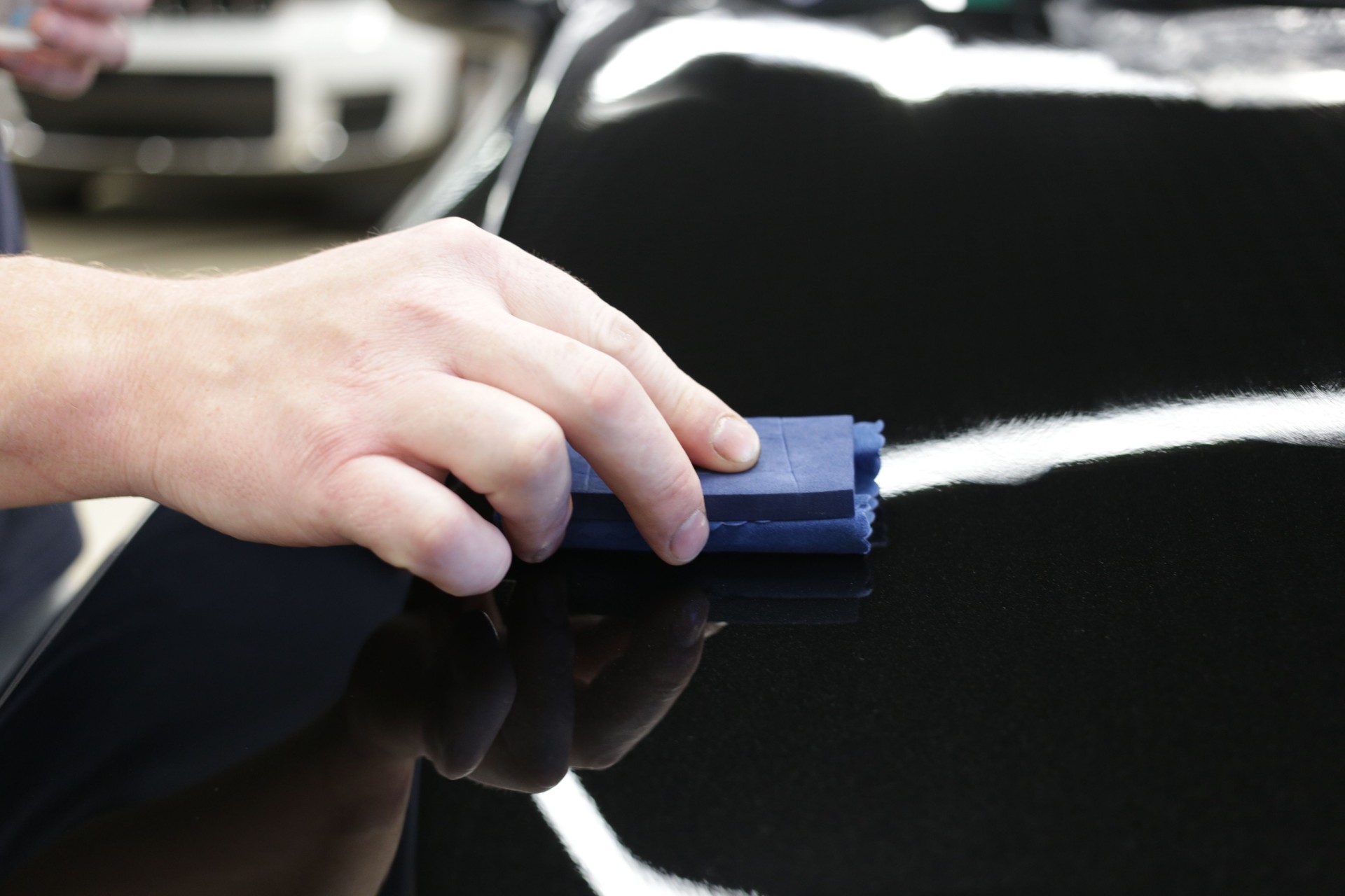 Car service worker applying nano coating on a car detail close-up. Closeup of hand coating black car bonnet paint.